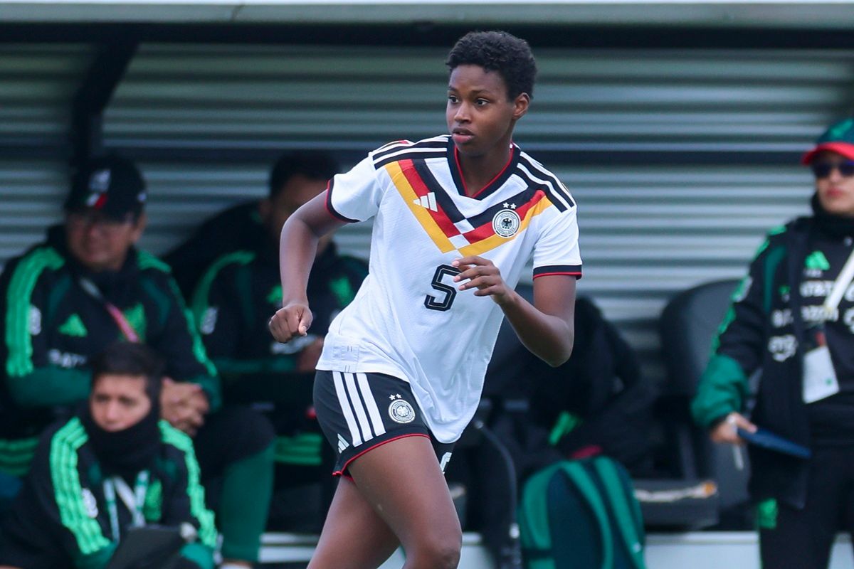 Eine Fußballspielerin in einem weißen Trikot mit farbigen Streifen bereitet sich auf den Einsatz während eines Spiels vor.