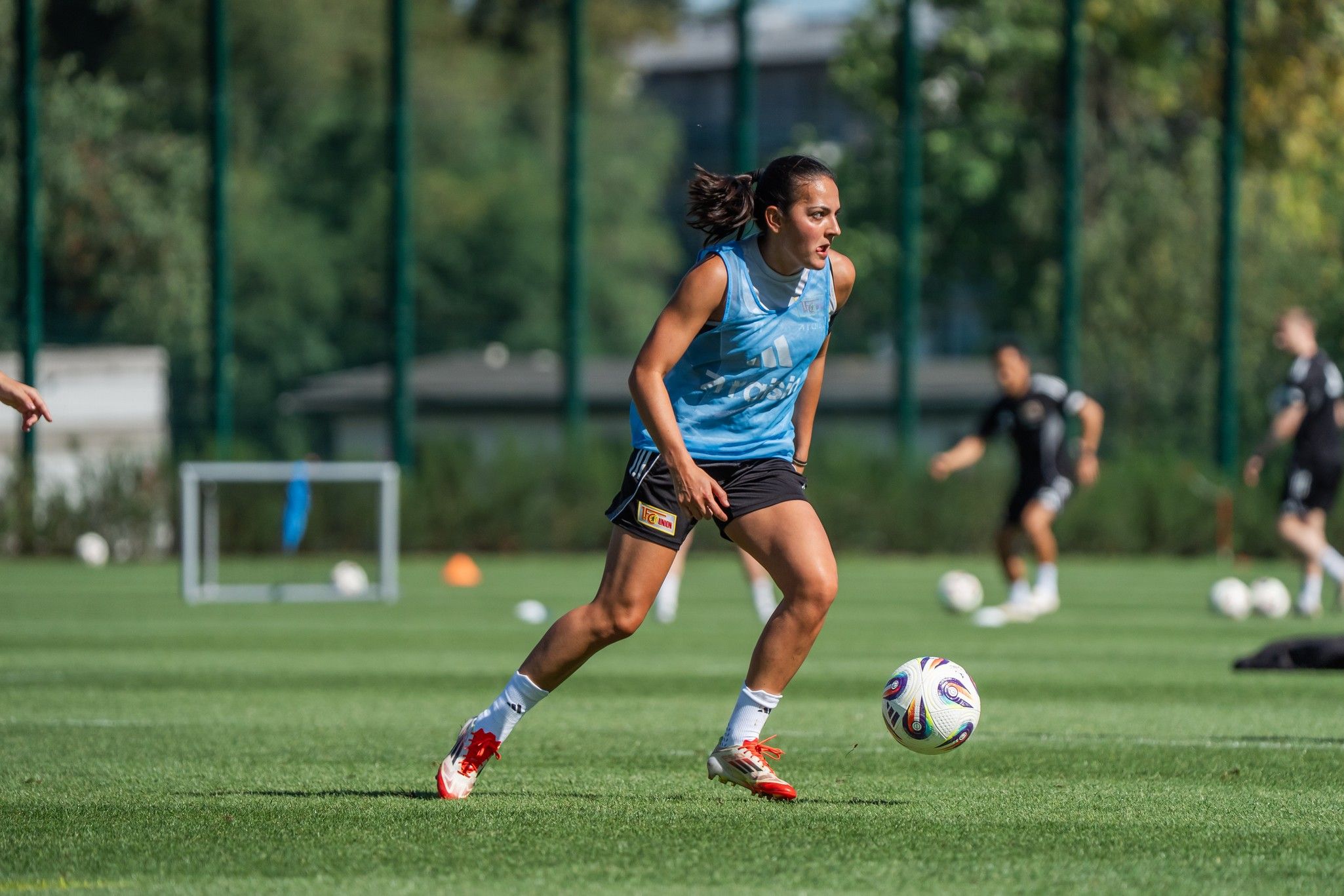Eine Fußballspielerin in einem blauen Trikot dribbelt den Ball während des Trainings auf einem grünen Fußballfeld.