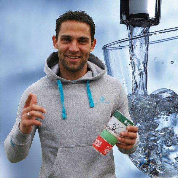 Mann in grauem Hoodie hält eine Dose in der einen Hand und zeigt mit der anderen Hand nach vorne vor einem Wasserhintergrund.