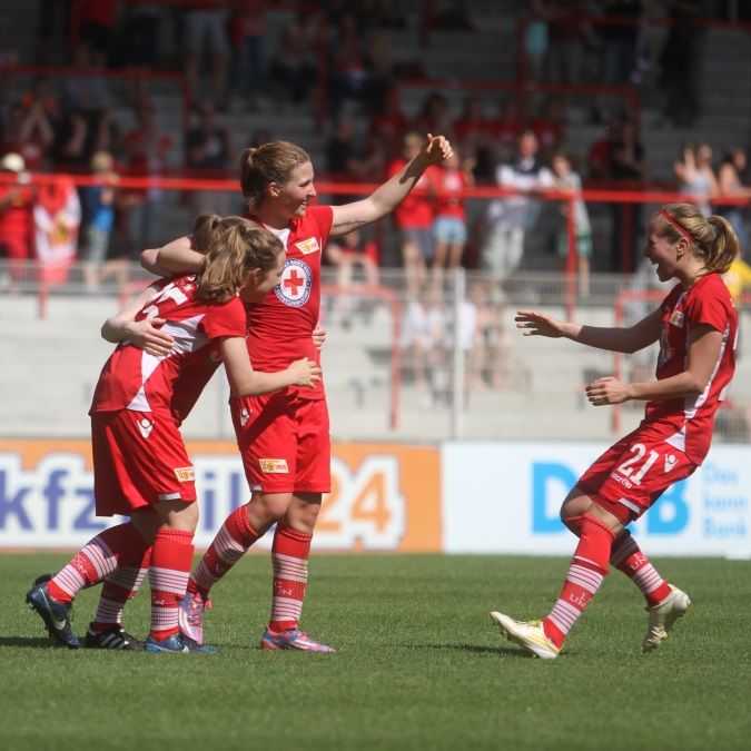 Vier Fußballspielerinnen in roten Trikots feiern einen Torerfolg auf dem Spielfeld.