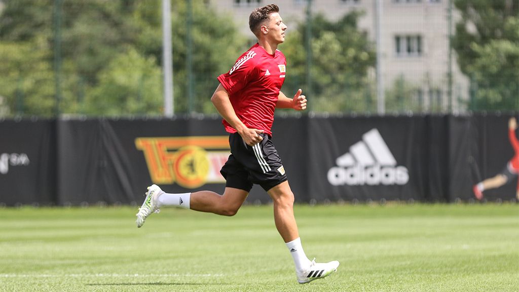 A young football player in a red jersey jogs on a training field.