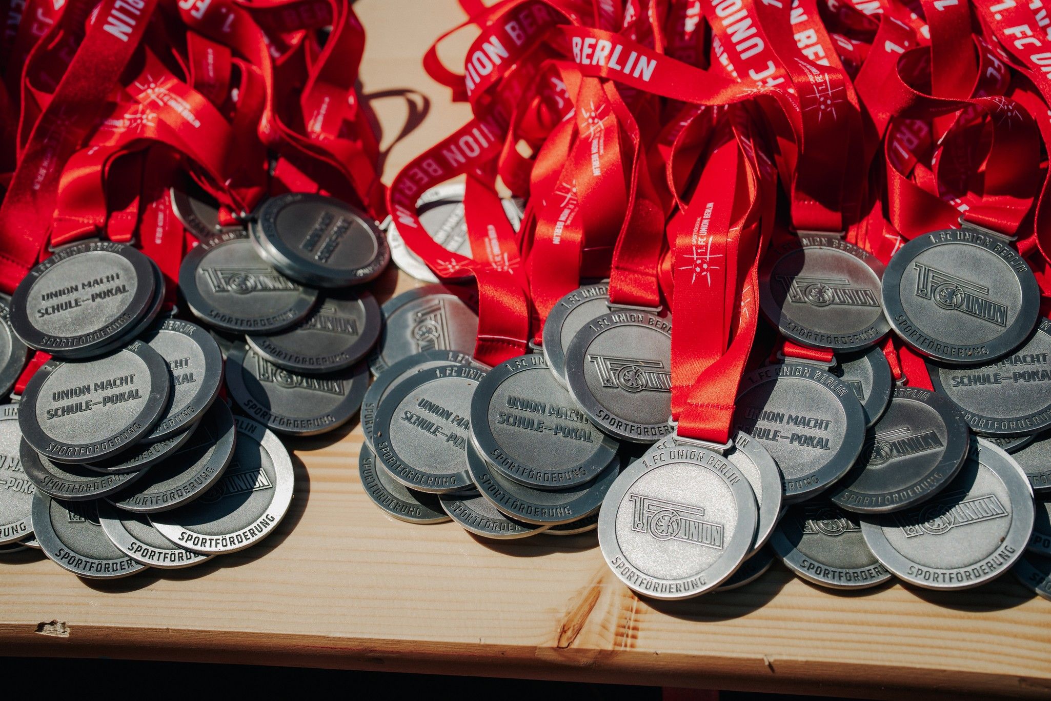 Eine Sammlung von silbernen Medaillen mit roten Bändern, die auf einem Holzuntergrund liegen.