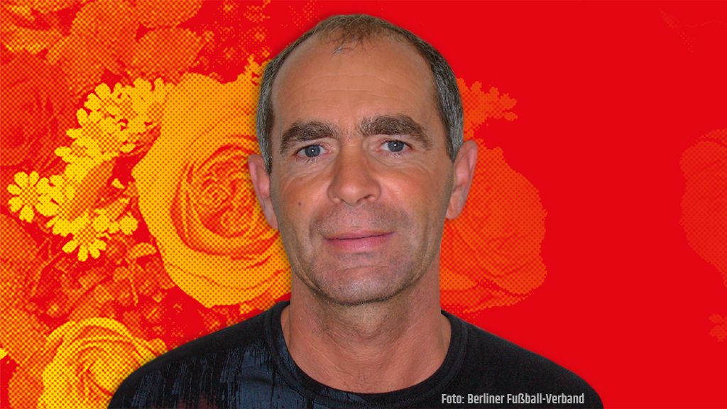 Porträt eines Mannes mit kurzen Haaren und ernstem Gesichtsausdruck vor einem roten Hintergrund mit Blumenmotiven.