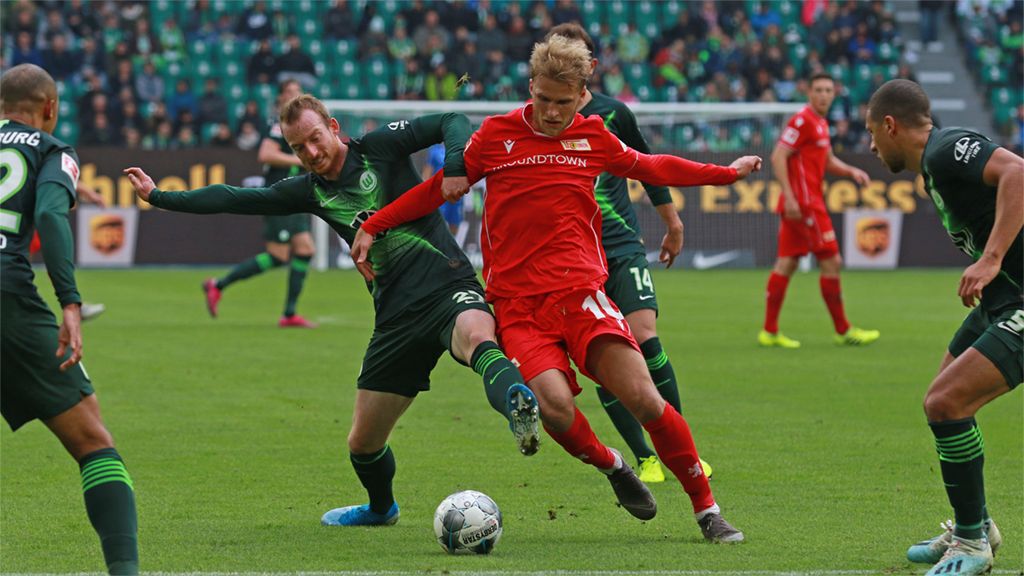 Ein Fußballspiel mit zwei Spielern im Wettkampf um den Ball, während Zuschauer im Hintergrund zu sehen sind.