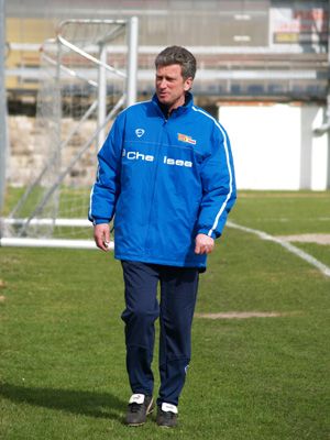 Eine Person in blauer Sportjacke und Hose läuft auf einem Fußballplatz. Im Hintergrund steht ein leeres Tor.