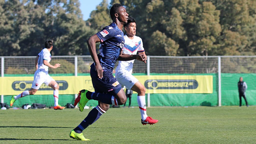 Soccer players are running on a green field, with one team in blue uniforms and the other in white.