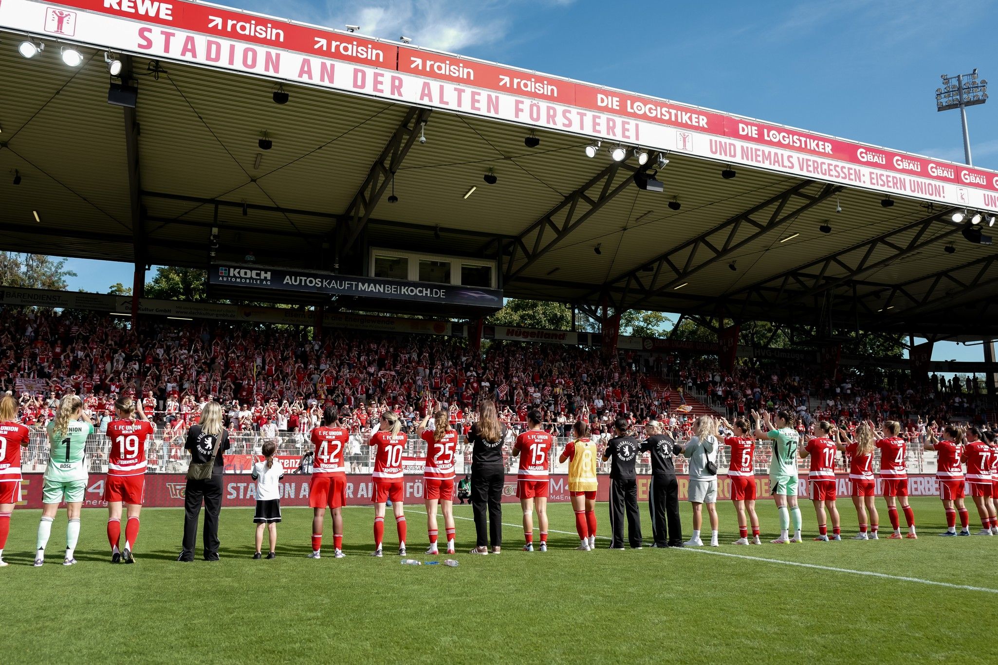 Spieler des Fußballteams stehen auf dem Platz im Stadion an der Alten Försterei, mit jubelndem Publikum im Hintergrund.