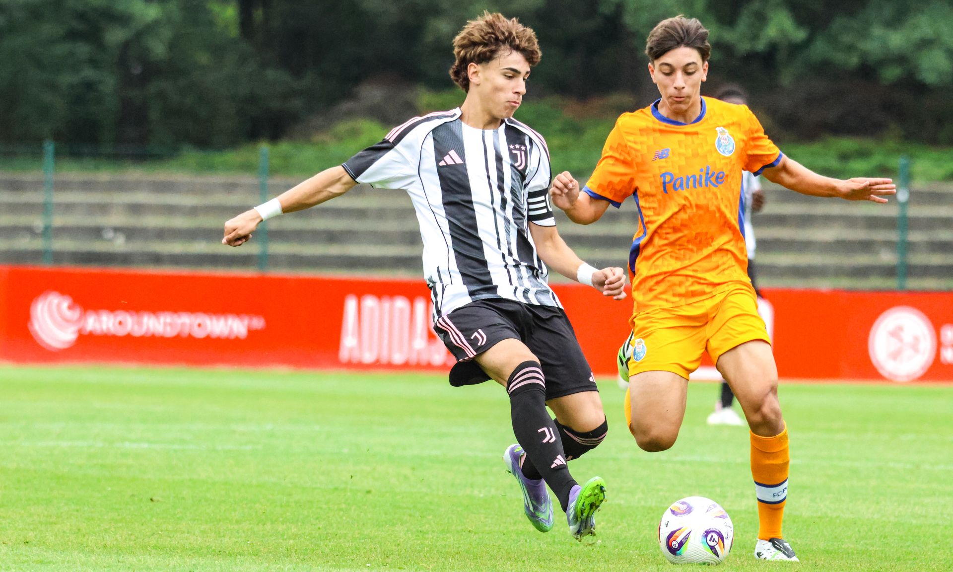 Zwei junge Fußballspieler in Action, einer in schwarz-weißer, der andere in orange-blauer Uniform, im Wettkampf um den Ball.
