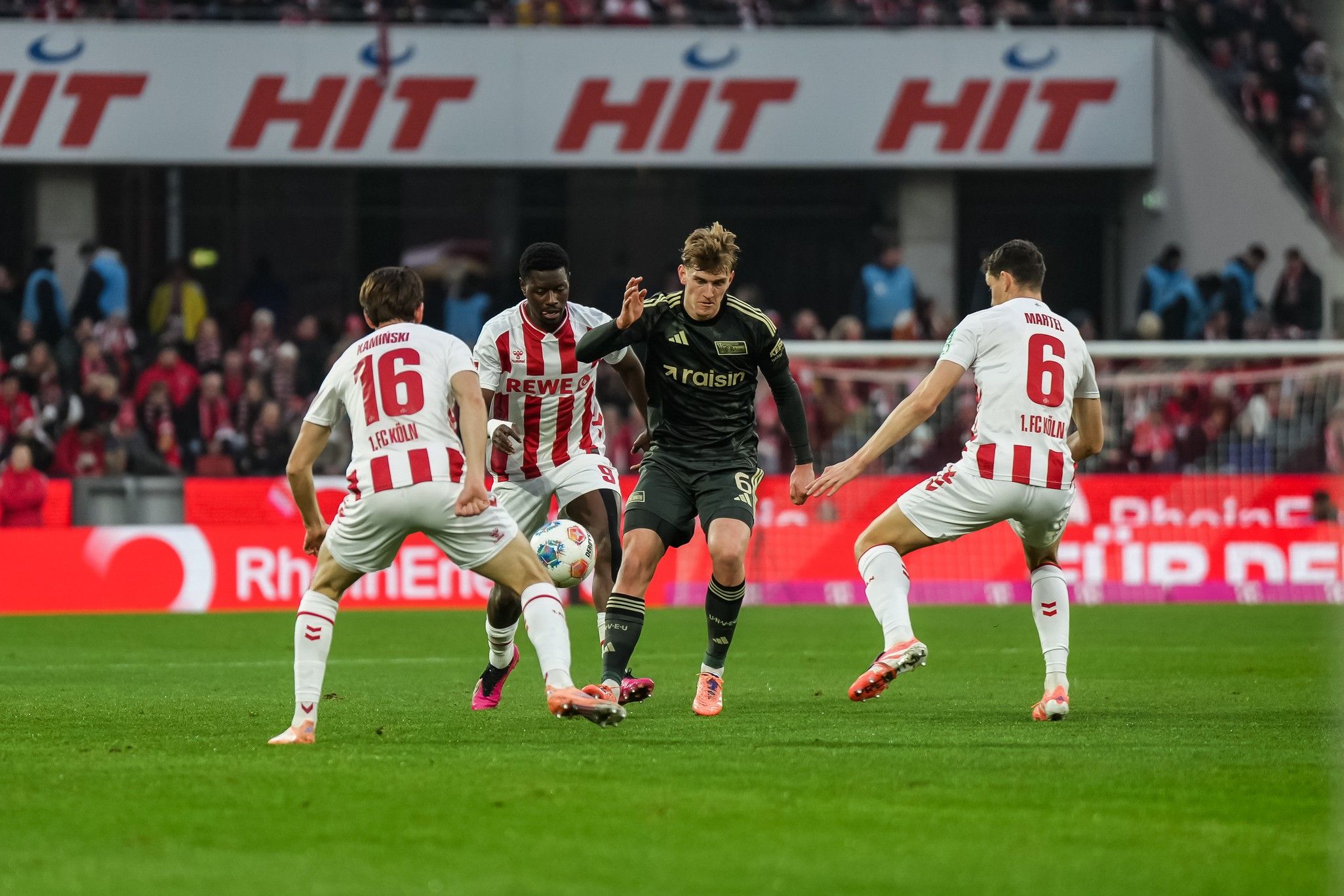 Ein Spieler in schwarzem Trikot umdribbelt zwei Verteidiger in weißen Trikots während eines Fußballspiels.