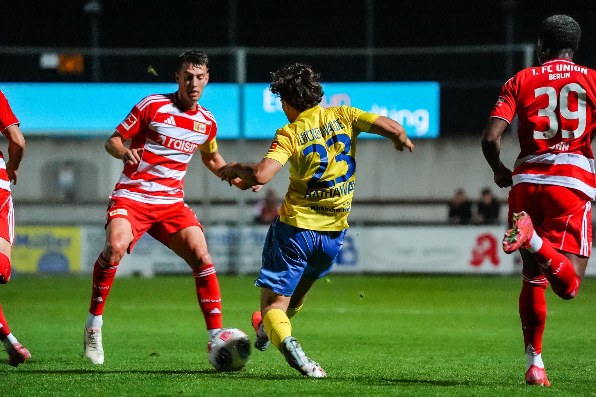 Ein Fußballspiel mit Spielern in roten und gelben Trikots, die im Wettkampf um den Ball sind.