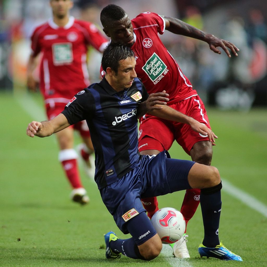 Ein Fußballspieler im blauen Trikot kämpft um den Ball gegen einen Spieler im roten Trikot.