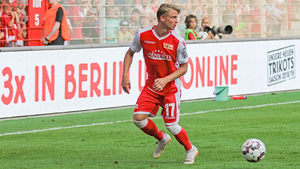 A soccer player in red team attire is dribbling the ball on the field in front of a lively crowd.