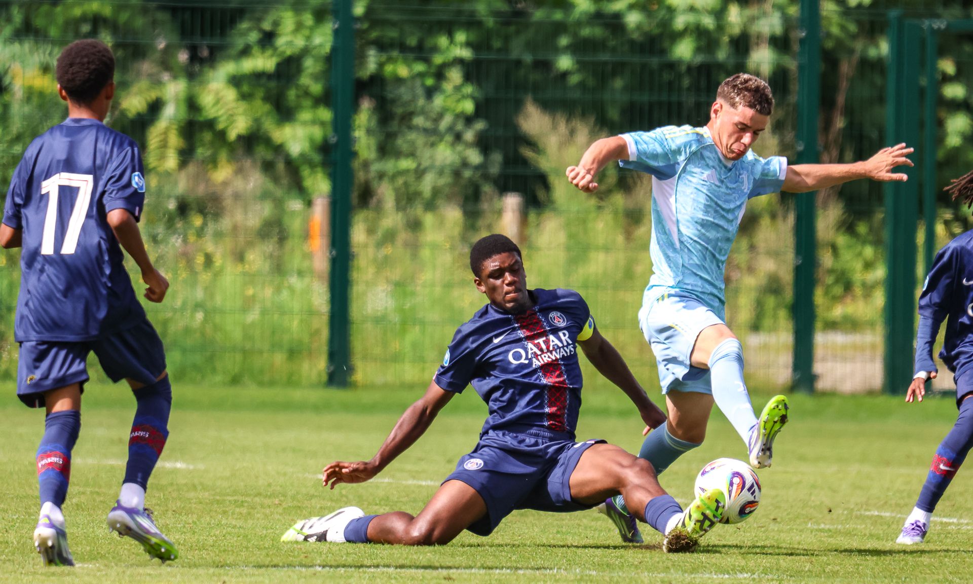 Spielszene eines Fußballspiels: Ein Spieler in blauer Uniform versucht, einen Gegner in hellblauer Kleidung zu foulen.