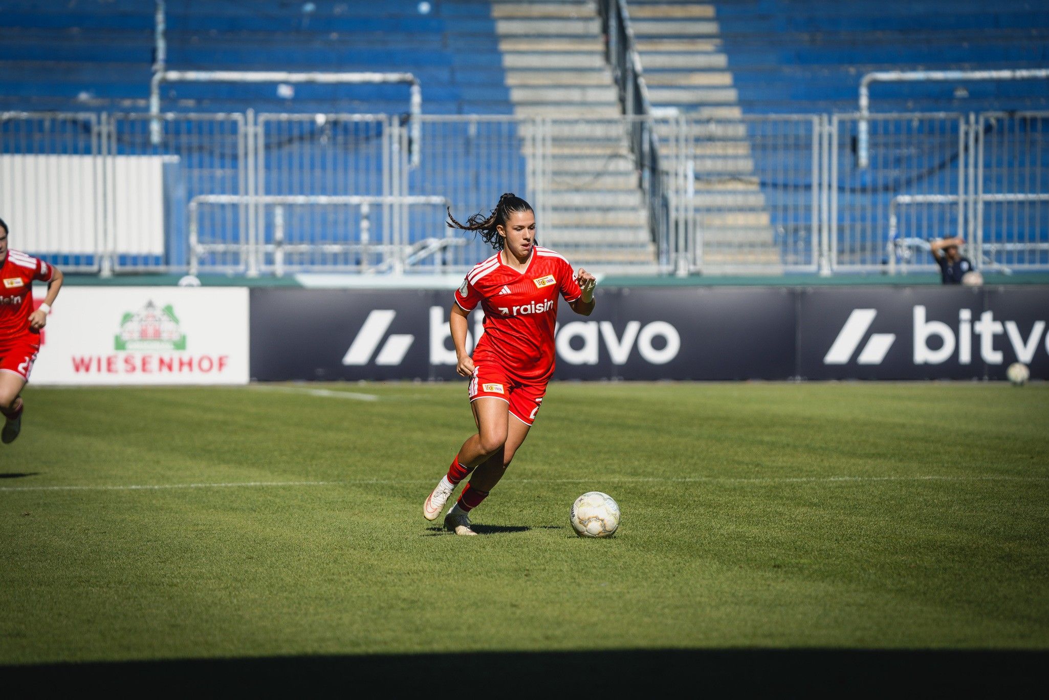 Eine Frau in rotem Fußballtrikot läuft mit dem Ball auf einem Spielfeld.