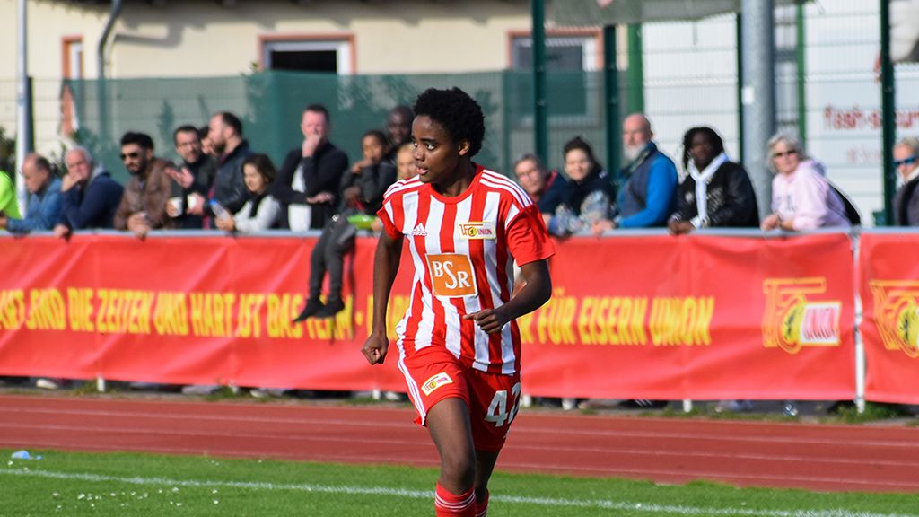 Soccer game: A player wearing the number 47 in a red and white striped jersey runs on a sports field, with spectators in the background.