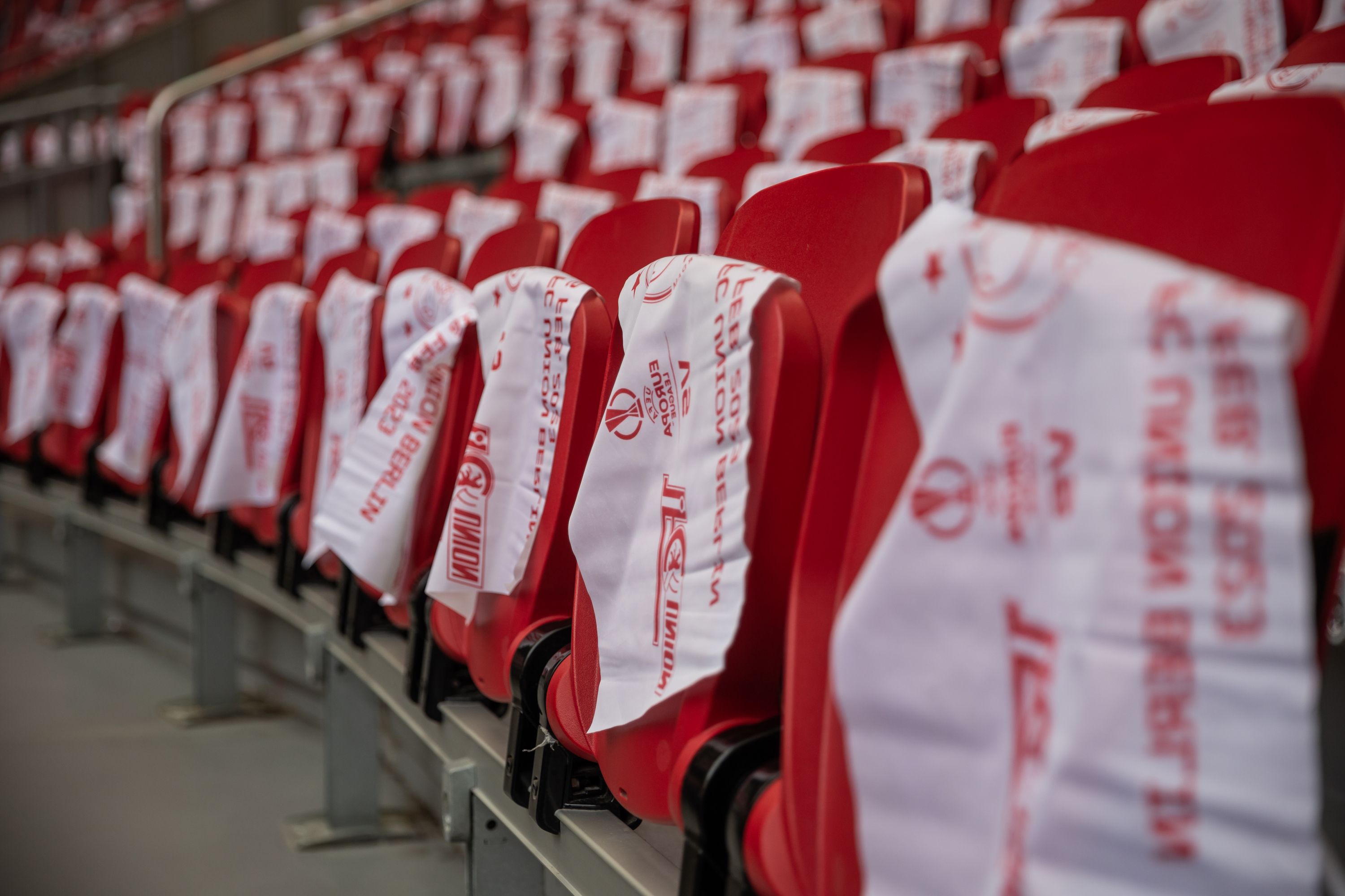 Row of red seats in a stadium, decorated with white towels hanging on the backs.