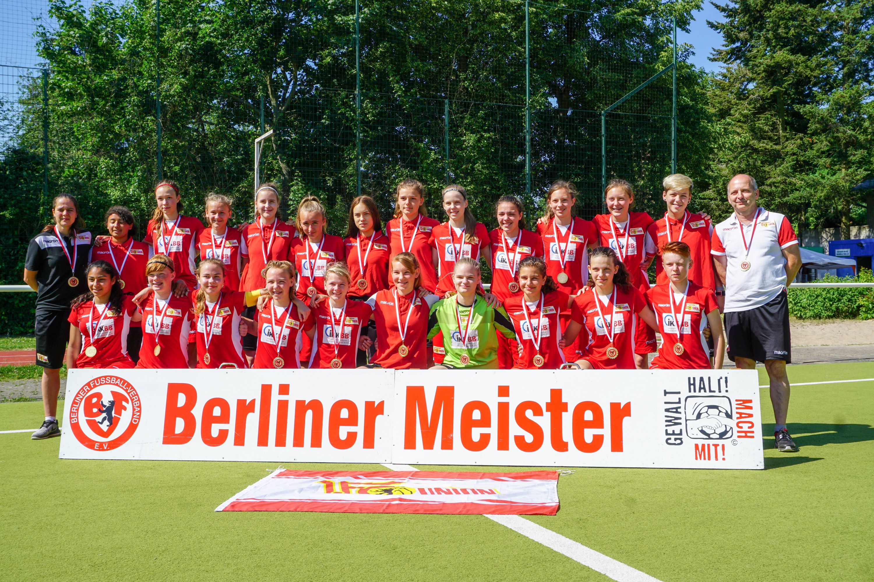 Gruppe von Mädchen in roten Fußballtrikots mit Medaillen, posieren vor einem Banner mit der Aufschrift "Berliner Meister".
