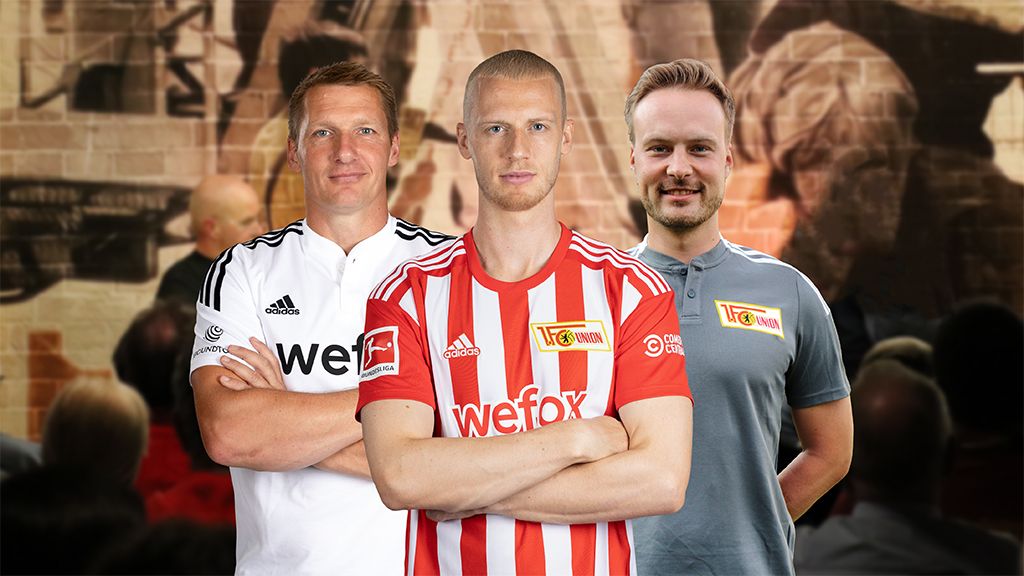 Drei Männer in Fußballtrikots stehen vor einer muralen Wand, lächelnd und mit verschränkten Armen.