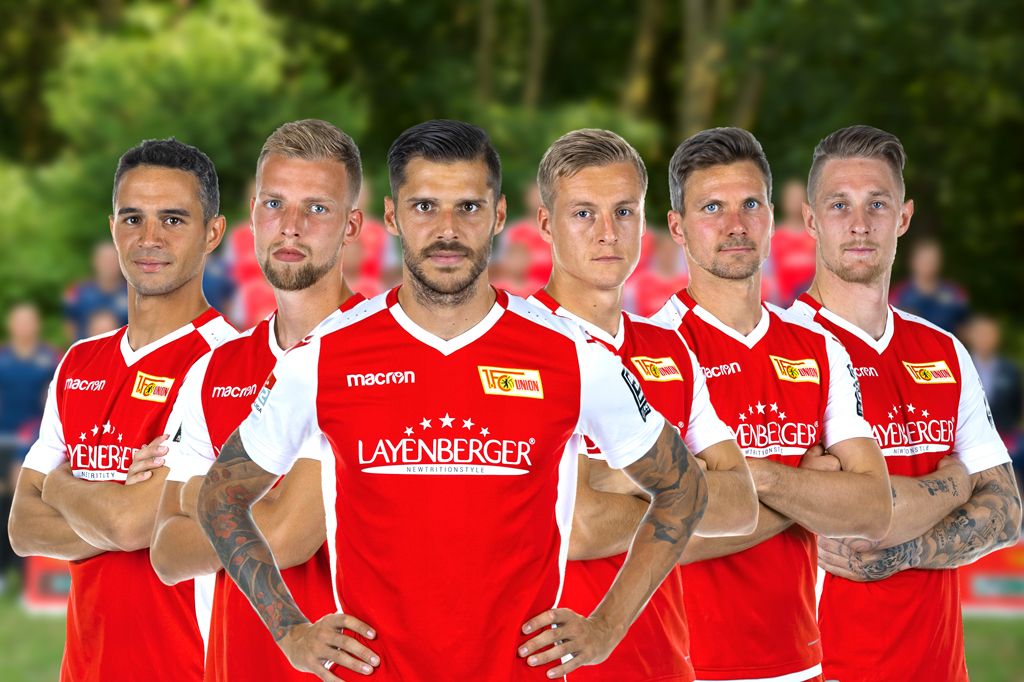 Sechs Fußballspieler in roten Trikots mit einem weißen Muster stehen nebeneinander und schauen in die Kamera.