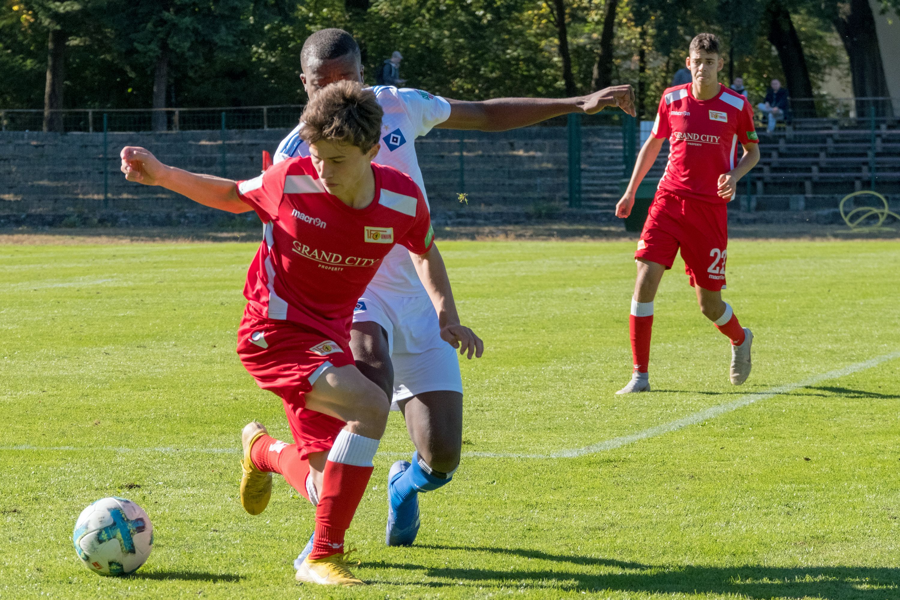 Zwei Fußballspieler in roten und weißen Trikots kämpfen um den Ball auf einem grünen Spielfeld.