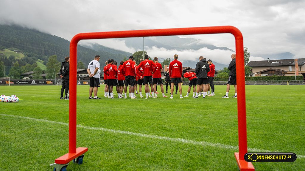 Sportmannschaft trainiert auf einem grünen Fußballfeld, mit einem mobilen Torrahmen im Vordergrund.