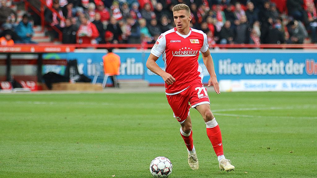 Ein Fußballspieler in rotem Trikot mit der Nummer 21 dribbelt über das Spielfeld während eines Spiels.