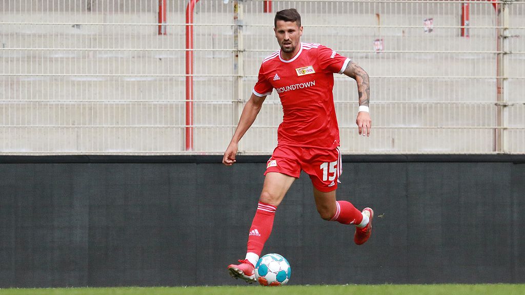 Ein Fußballspieler in rotem Trikot dribbelt den Ball auf einem Stadionrasen.