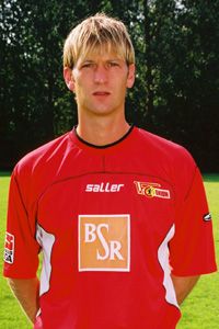 Ein junger Mann in einem roten Fußballtrikot steht vor einem grünen Hintergrund.