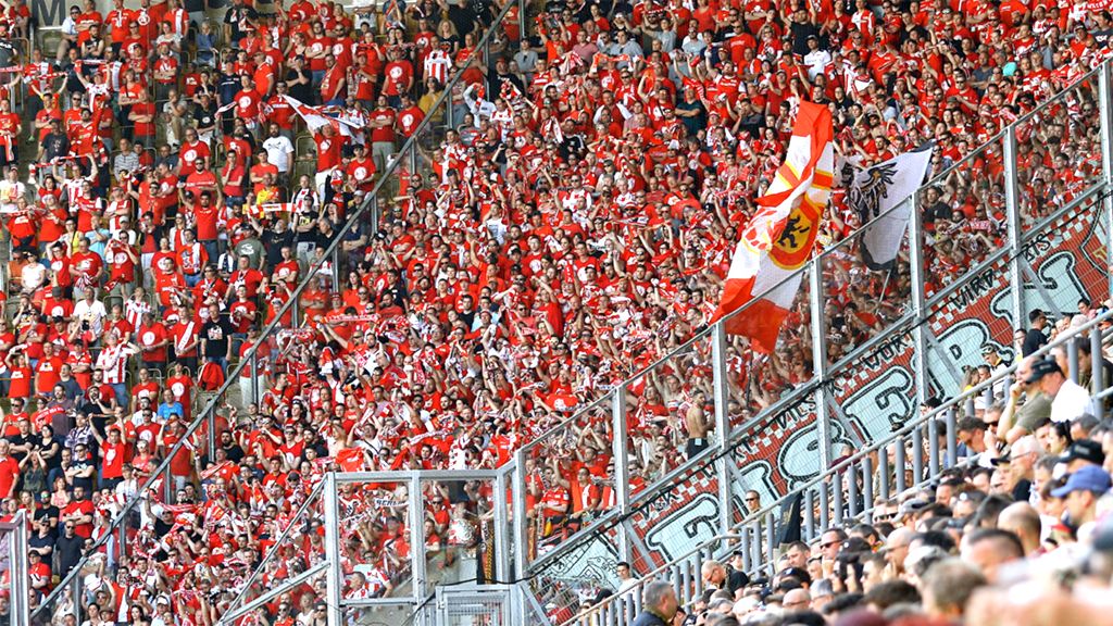 A cheering crowd in a stadium, dressed in red and white, with flags and scarves.