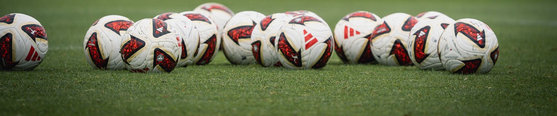 Eine Kollektion von Fußball mit roten und schwarzen Mustern, auf grünem Rasen angeordnet.