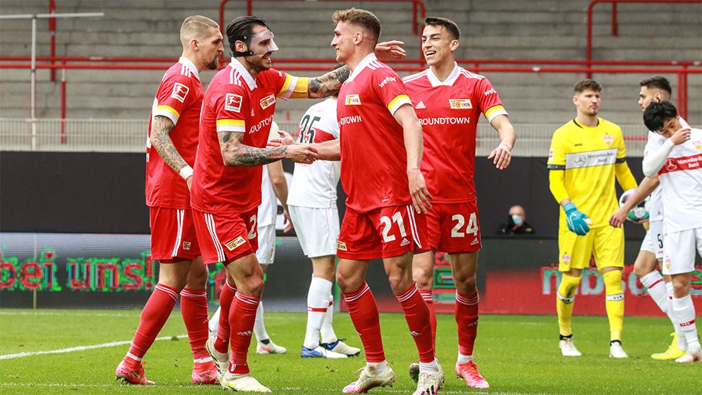 Fünf Fußballspieler in roten Trikots feiern einen Torerfolg auf dem Spielfeld. Im Hintergrund steht ein Torwart in gelber Kleidung.