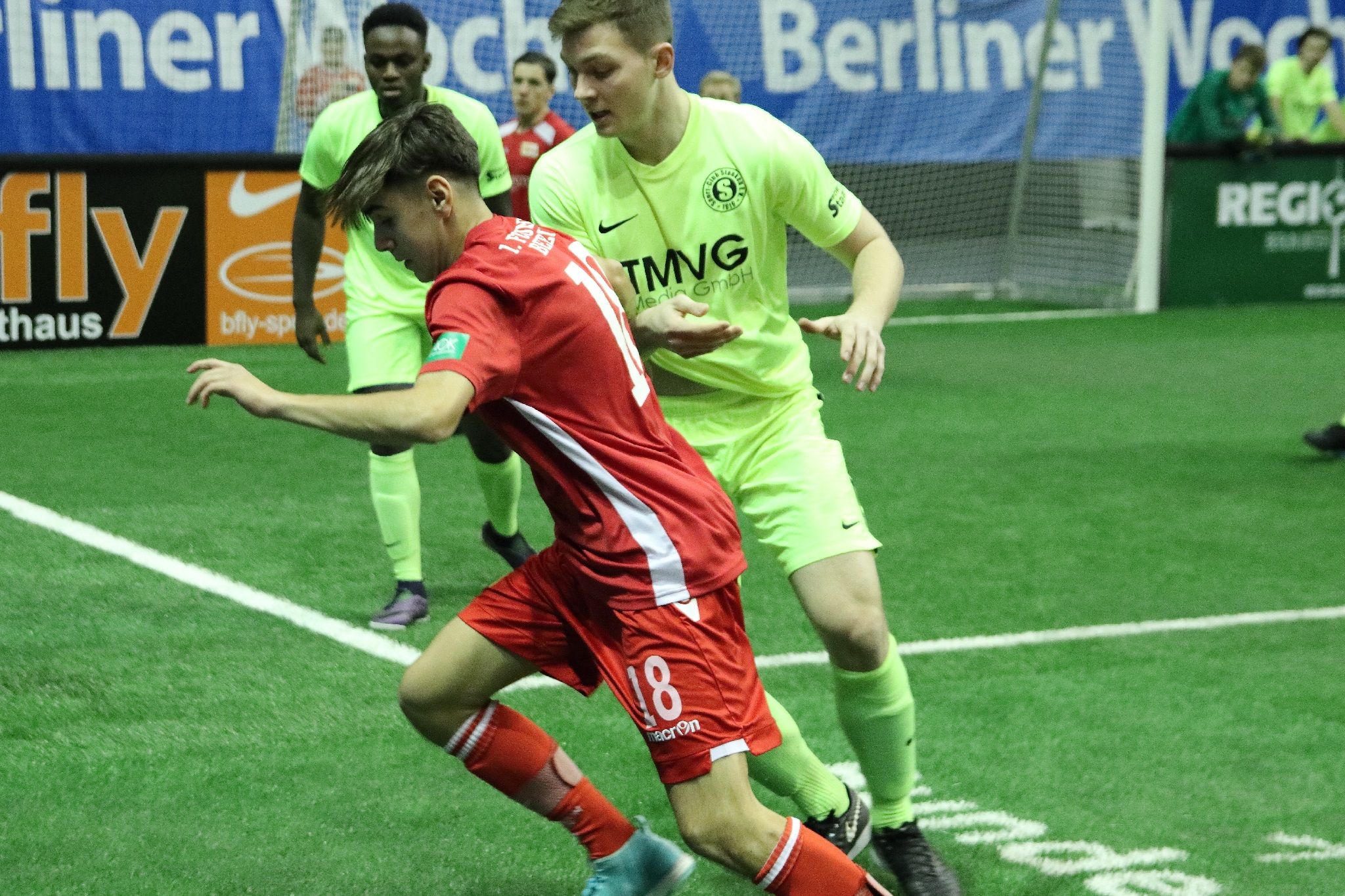 Ein Fußballspiel mit zwei Spielern in Aktion, der eine trägt ein rotes Trikot, der andere ein grünes.