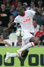 Ein Fußballspieler springt, um den Ball zu verhindern, während Zuschauer im Hintergrund zuschauen.