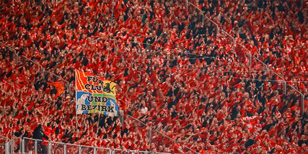 An enthusiastic crowd in red jerseys waving a colorful flag and cheering the atmosphere.