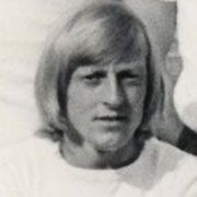 Porträt eines jungen Mannes mit blonden, schulterlangen Haaren, der direkt in die Kamera schaut.