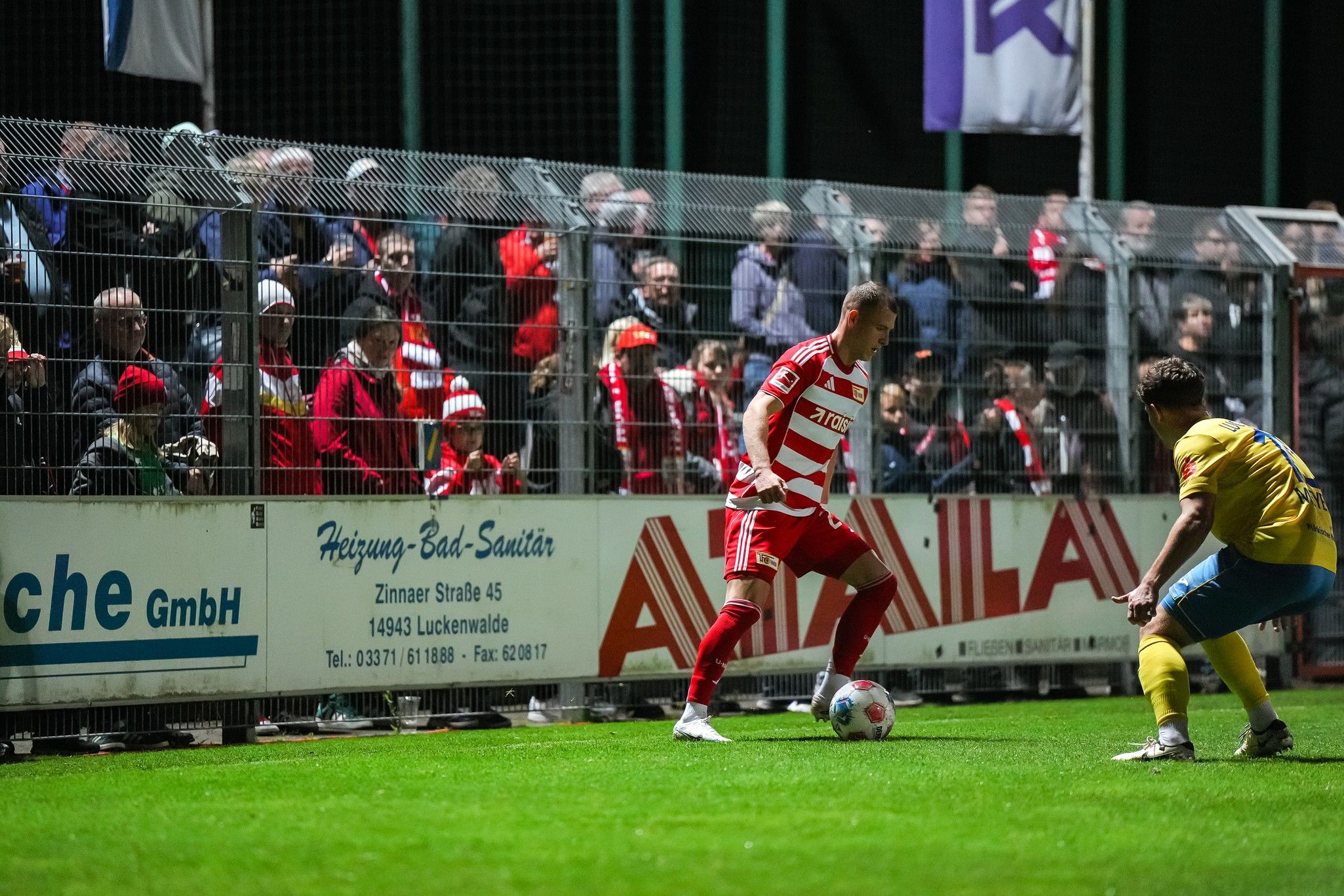 Ein Fußballspieler dribbelt den Ball an der Seitenlinie, während Zuschauer im Hintergrund stehen.