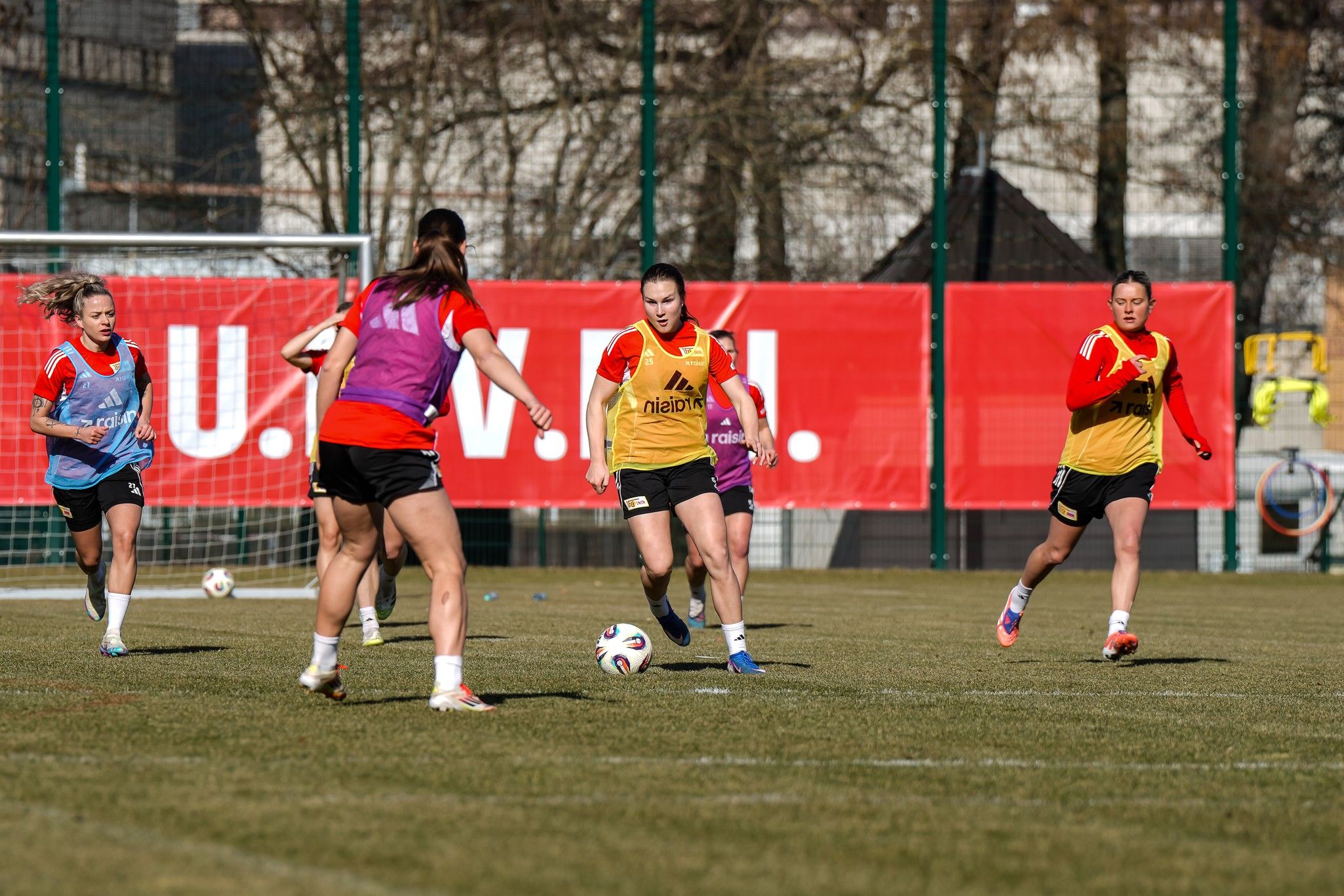 Frauenfußballmannschaft trainiert auf einem Rasenplatz, Spielerinnen dribbeln und passen den Ball.