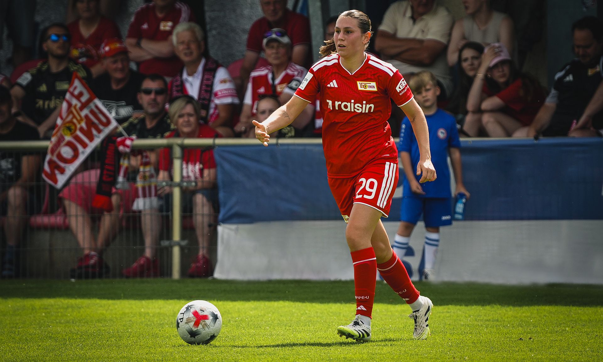 Spielerin in rotem Trikot mit der Nummer 29 läuft auf dem Fußballfeld, im Hintergrund Zuschauer mit Fanschals.