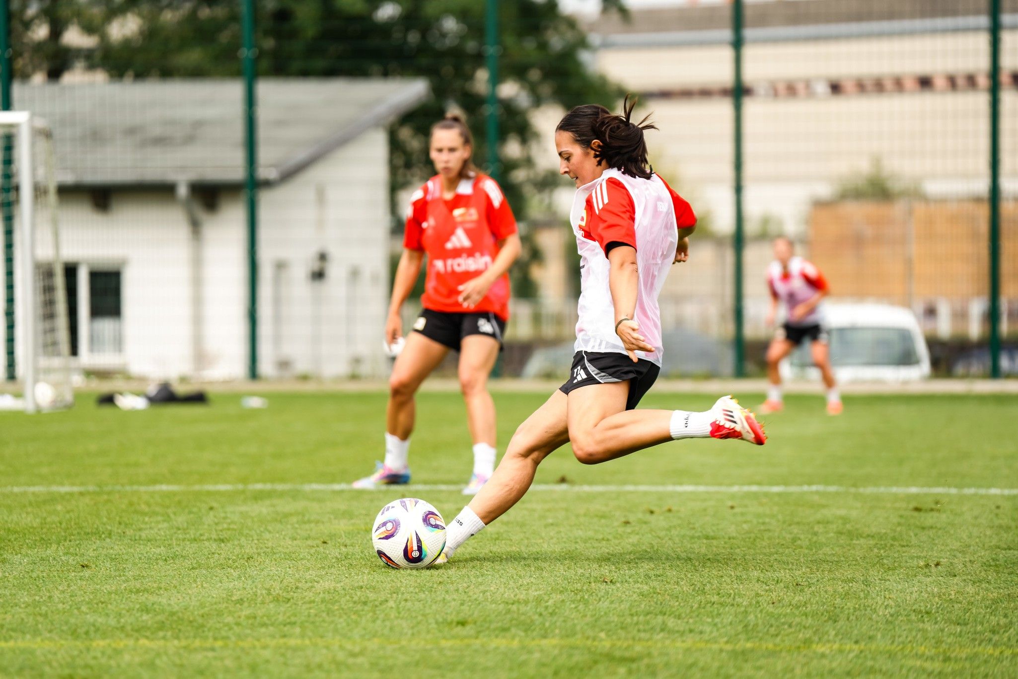 Eine Fußballspielerin tritt den Ball während des Trainings, während eine andere Spielerin im Hintergrund zuschaut.