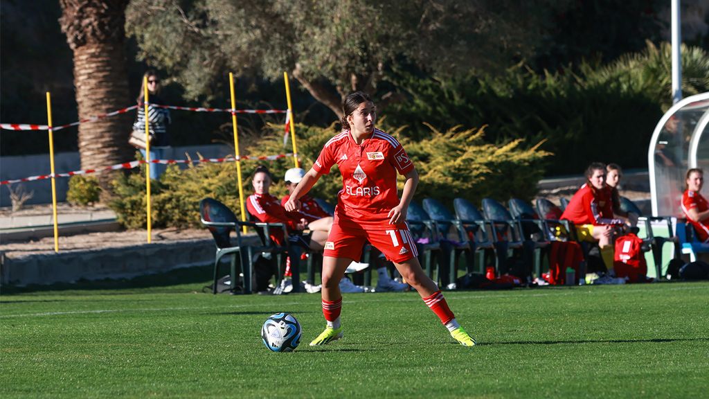 Spielerin in rotem Trikot mit der Nummer 7 bereitet sich auf einen Freistoß auf einem Fußballfeld vor.