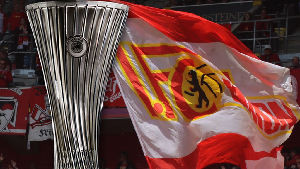 Das Bild zeigt einen großen Pokal vor einer wehenden Flagge mit dem Logo von Union Berlin.