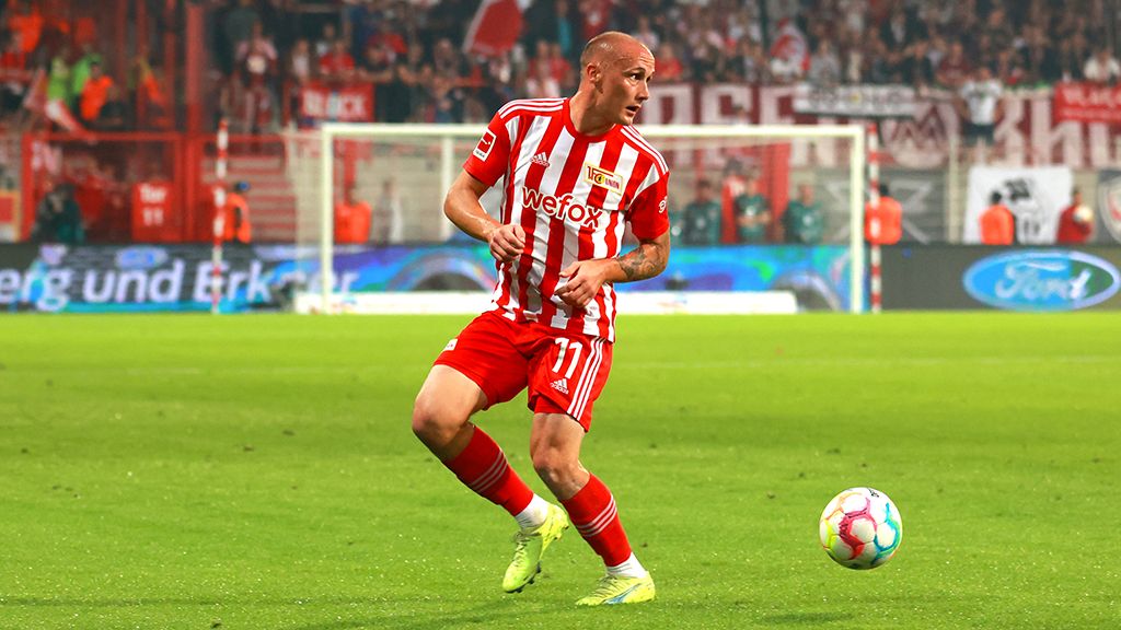 A football player in a red-and-white kit dribbles the ball on the field during a game.