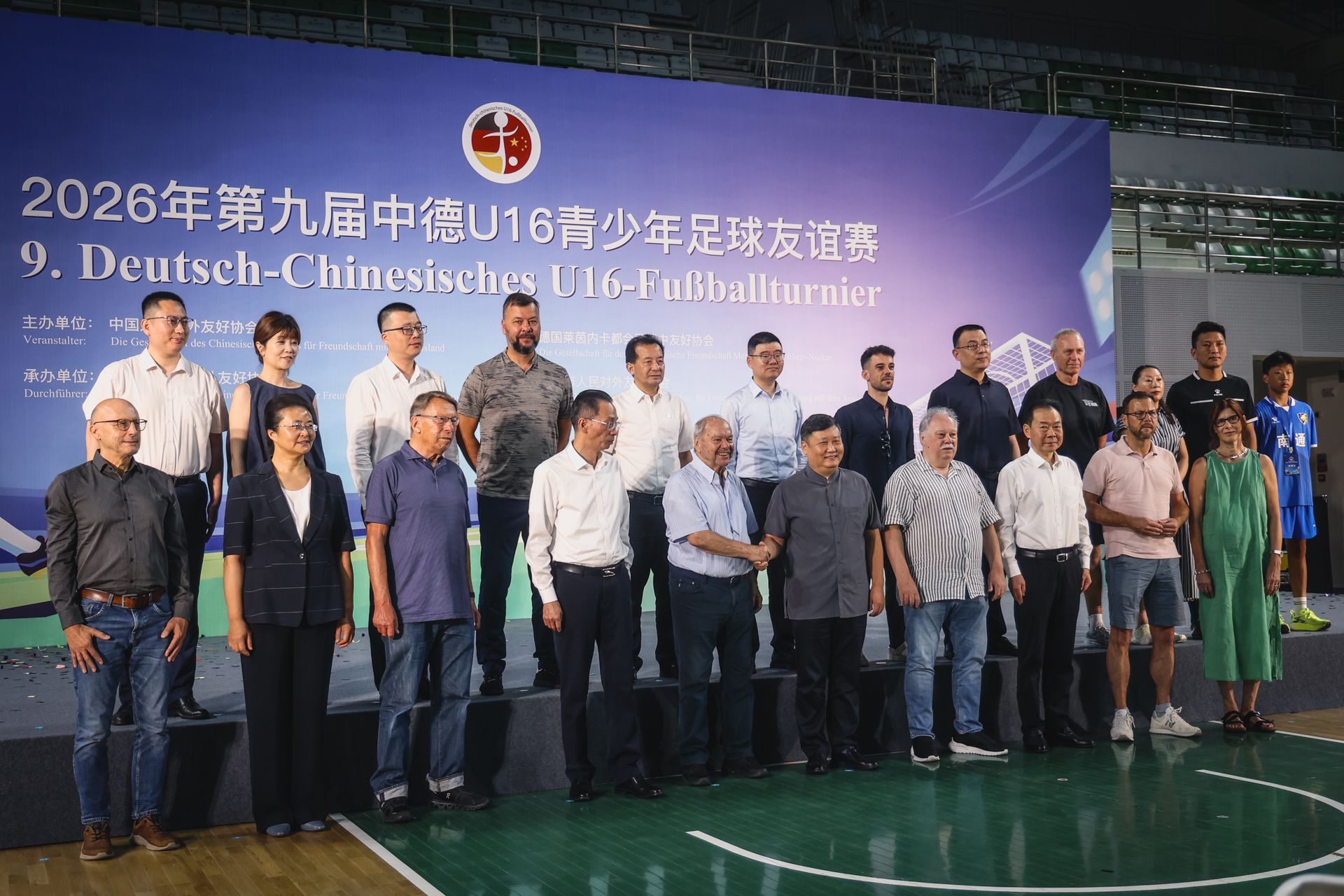 Menschen stehen auf einer Bühne vor einem Banner, das das 9. Deutsch-Chinesische U16-Fußballturnier ankündigt.