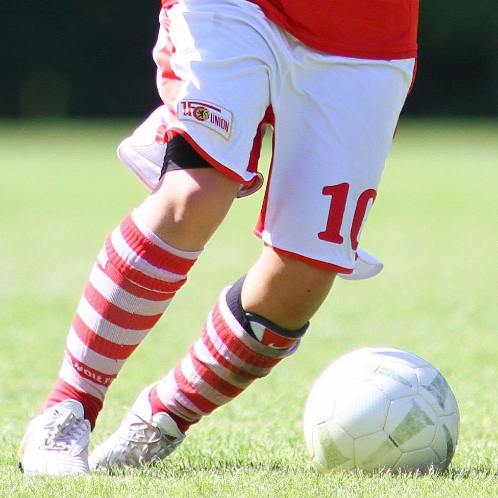 Ein Fußballspieler in roten und weißen Trikots dribbelt einen Fußball auf einem grünen Rasenfeld.