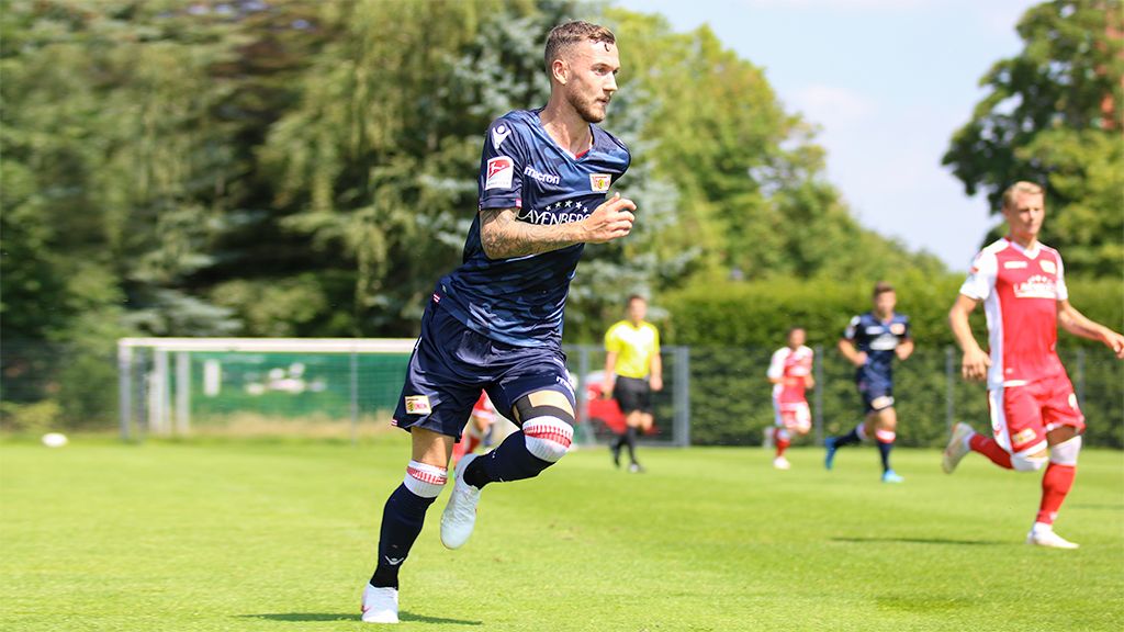Fußballspieler in blauer Uniform sprintet über das Feld, während eine Partie im Hintergrund gespielt wird.