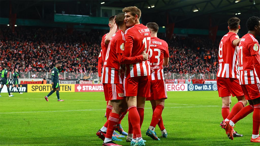 Spieler des 1. FC Union Berlin feiern einen Torerfolg in einem Stadion mit jubelnden Fans im Hintergrund.