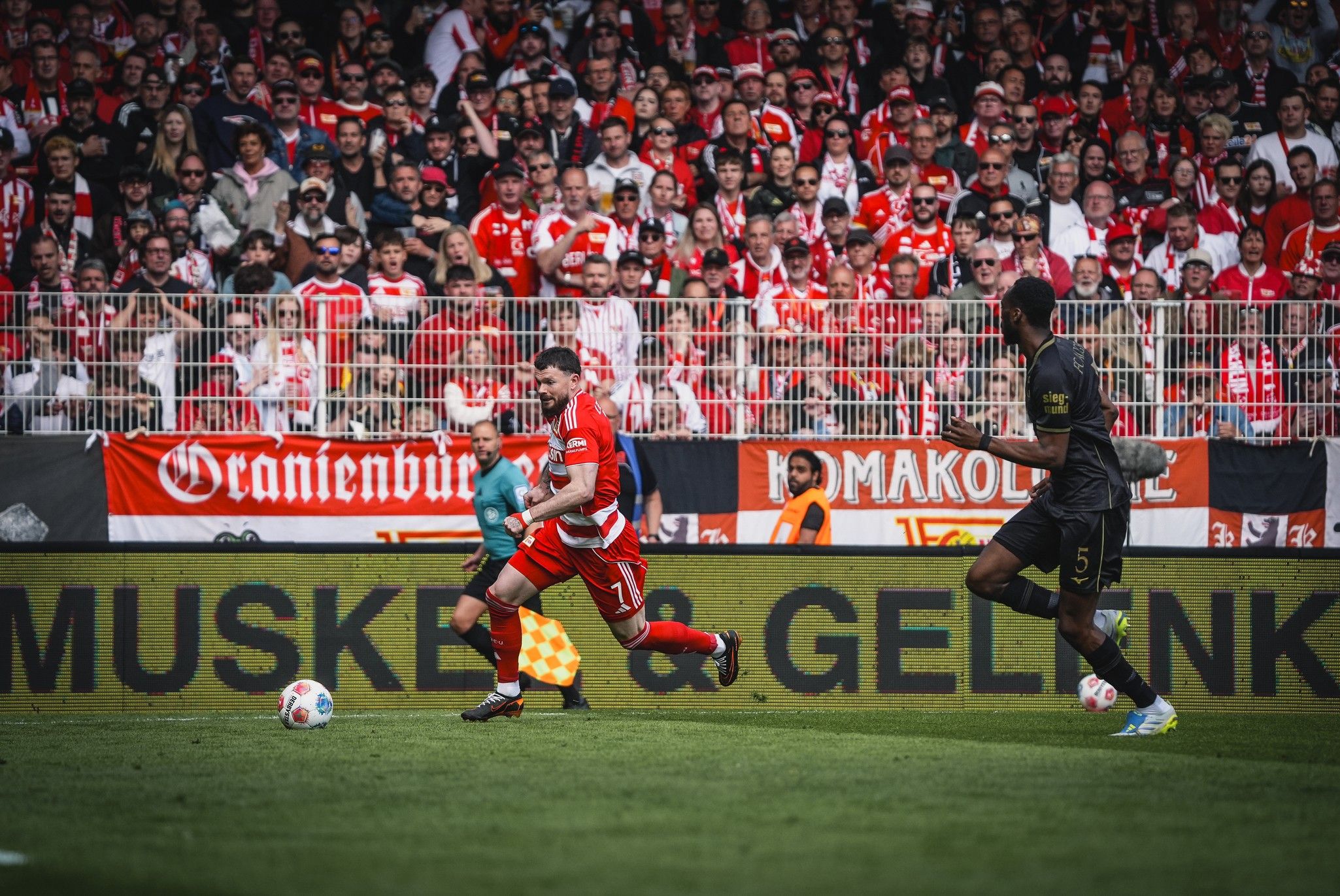 Ein Fußballspieler sprintet auf dem Feld, während die Zuschauermenge in der Wüste jubelt.