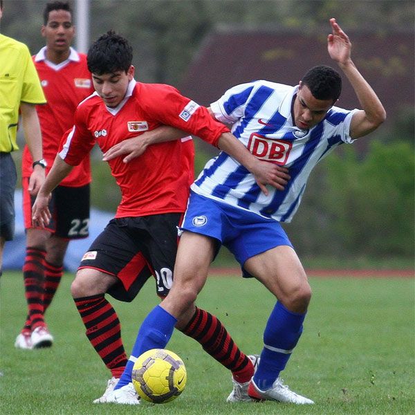 Zwei Fußballspieler kämpfen um den Ball auf einem Rasenplatz während eines Spiels.
