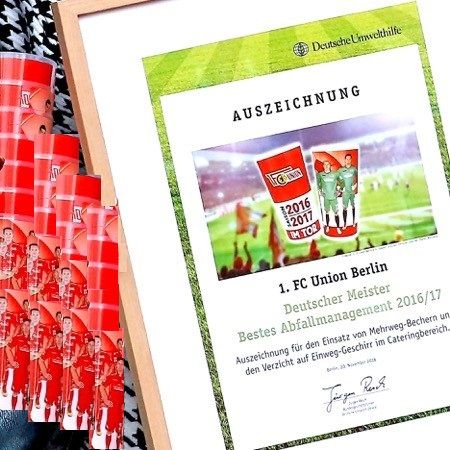 Urkunde des 1. FC Union Berlin für das beste Abfallmanagement 2016/17, umgeben von roten Mehrweg-Bechern.