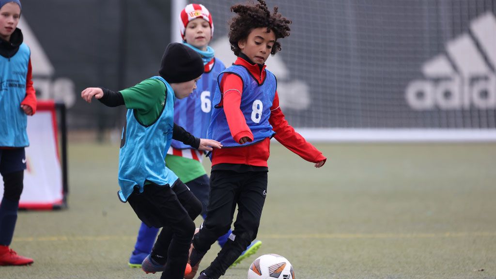 Zwei Kinder spielen Fußball auf einem Sportplatz. Eines dribbelt den Ball, während das andere versucht, ihn zu erobern.